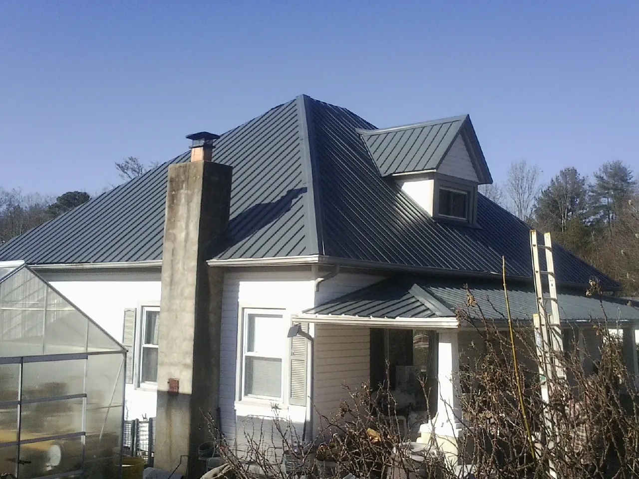 Dark blue standing seam metal roof on a white farmhouse with dormer — Slate & Tile Roof Repair by Roofing Brothers in Verona